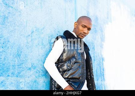 Bel maschio afro-americano calvo in abbigliamento elegante guardando la macchina fotografica mentre si trova vicino al muro sulla strada della città Foto Stock