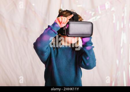 Bambino in moderni occhiali VR vivere la realtà virtuale in studio su sfondo lucido con luci al neon Foto Stock