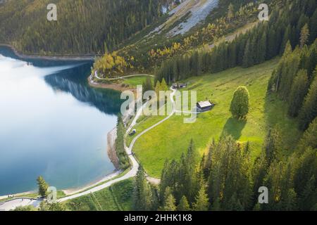 Paesaggio aereo di piccoli cottage situato sul verde prato pendio di montagna vicino lago tranquillo circondato da foresta conifere in giorno di sole Foto Stock