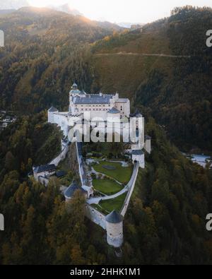Vista con droni di un antico castello in pietra situato in un terreno collinare coperto da rigogliosi boschi di conifere nella città di Salisburgo in Austria Foto Stock