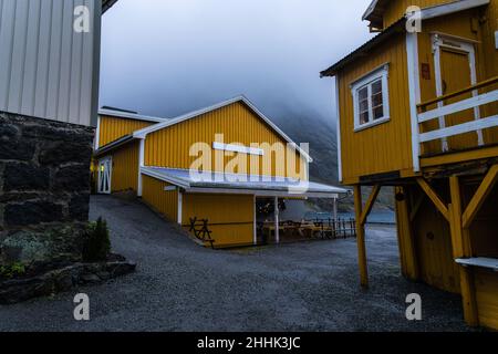 Tipiche piccole case gialle situate vicino al mare circondate da montagne nascoste sotto il cielo di nebbia nel villaggio di Nusfjord in Norvegia Foto Stock