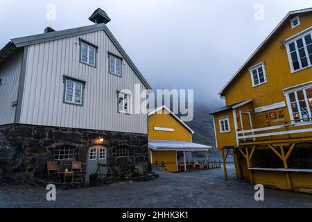 Tipiche piccole case gialle situate vicino al mare circondate da montagne nascoste sotto il cielo di nebbia nel villaggio di Nusfjord in Norvegia Foto Stock