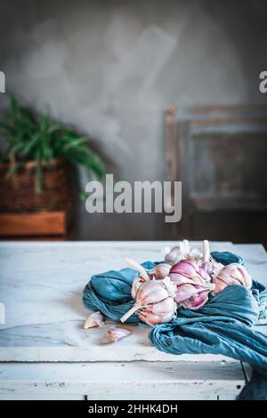 Spicchi di aglio non pelato serviti con tovagliolo blu e piatto di ceramica posto sul tavolo in cucina leggera Foto Stock