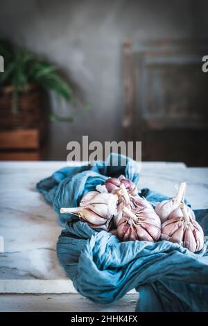 Spicchi di aglio non pelato serviti con tovagliolo blu e piatto di ceramica posto sul tavolo in cucina leggera Foto Stock