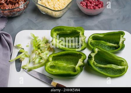 Da sopra di peperoni verdi freschi tagliati sul tagliere con coltello sistemato sul tavolo con carne e formaggio per farcire la pizza Foto Stock
