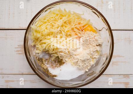 Vista dall'alto del recipiente di vetro con farina e formaggio grattugiato per il chaffle di zucca posto su un tavolo di legno in cucina leggera Foto Stock