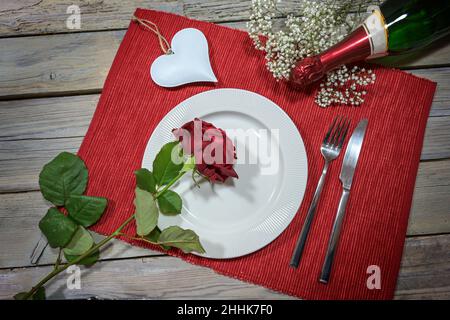 Cena romantica di San Valentino, piatto bianco con una rosa rossa, a forma di cuore e una bottiglia di champagne su un tovagliolo e un rustico tavolo in legno, concetto di amore, h Foto Stock