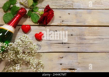 Invito romantico con champagne, rosa rossa e due cuori su sfondo rustico in legno, concetto d’amore per San Valentino, spazio copia, angolo alto vi Foto Stock
