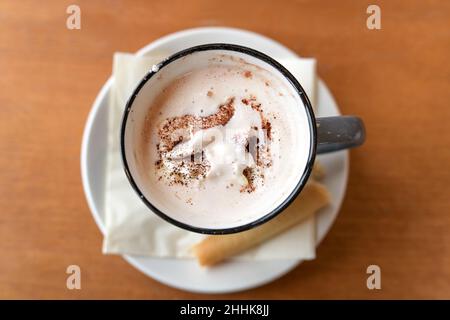 Bevanda calda al cioccolato con panna montata e polvere di cacao servita con un biscotto in una tazza su un tavolo di legno, spazio copia, vista ad angolo alto dall'alto, selec Foto Stock