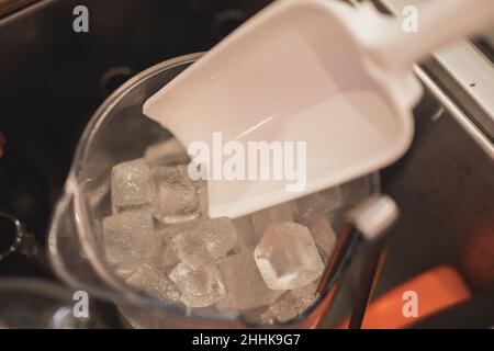 Persona anonima ad alto angolo di raccolto che prende i cubetti di ghiaccio dalla caraffa per preparare la bevanda fredda nel bar Foto Stock