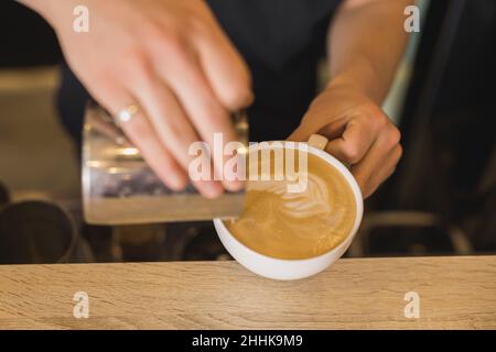 Da sopra di raccolto anonimo barista maschio versando il latte dalla caraffa in tazza di cappuccino mentre si fa latte arte in caffè Foto Stock