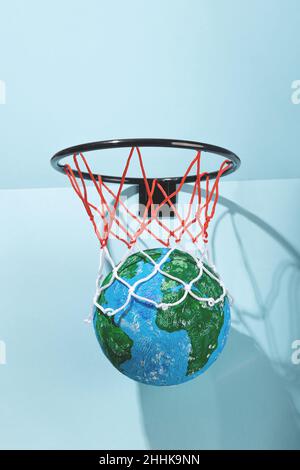Pianeta rotondo Terra con acqua e terra in basket con rete colorata su sfondo chiaro con luce solare e ombra Foto Stock