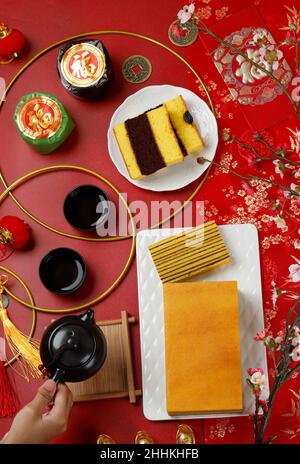 Concept Flat Lay Chinese New Year Dessert, Nian Gao Kue Keranjang, Lapis Legit torta stratificata, tè, e Spiku Lapis Surabaya, femmina mano tenere Teapot. C Foto Stock