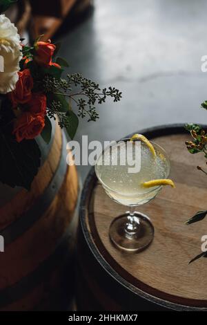 cocktail ghiacciato in champagne coupé di vetro stemware con scorza di limone guarnire su barile di whiskey Foto Stock