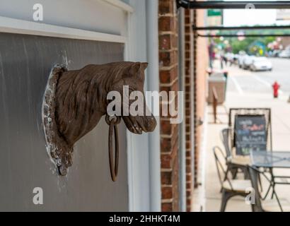 Old Antique Vintage Metal Horse Head and Ring attaccato al muro di edificio con marciapiede, strada e auto sfocate in lontananza. Foto Stock