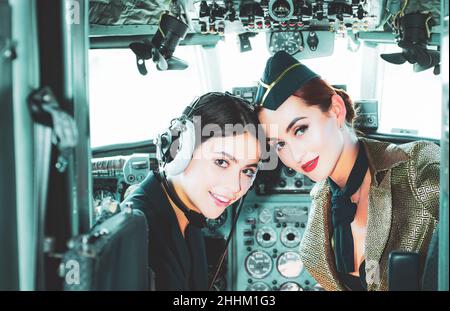Due donne piloti seduti in cabina di velivolo moderno. Sorridente stewardess nel velivolo. Ritratto di attraente donna trainee pilota con cuffia Foto Stock
