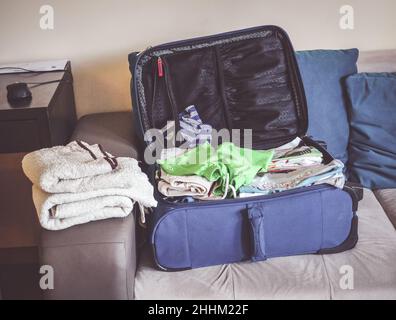 Primo piano di una valigia blu piena di vestiti sdraiati sul divano pronto prima di un viaggio Foto Stock