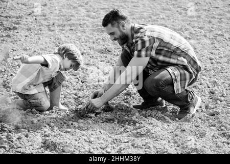 Padre e figlio lavorano sulla terra. Famiglia che pianta. Papà che insegna il ragazzino a fare il giardinaggio. Foto Stock