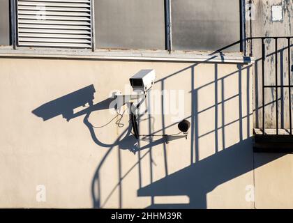 Telecamera professionale CCTV che guarda fuori con il getto d'ombra sulla parete dell'edificio. Area ad alta sicurezza con telecamera a circuito chiuso e scala industriale Foto Stock