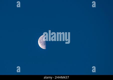 Mezza luna alta contro il cielo blu nuvoloso della mattina presto Foto Stock