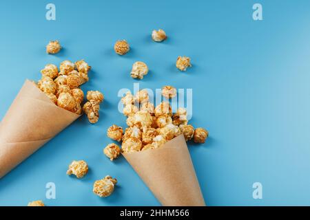 Popcorn in caramello glassa in una busta di carta su uno sfondo blu. Un'ottima lode per guardare film, serie, cartoni animati. Spazio libero, vista dall'alto. Foto Stock