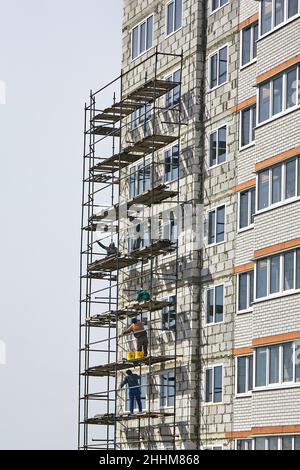 Installazione del ponteggio. I costruttori lavorano senza mezzi di protezione, assicurazione. Lavori di costruzione e installazione. Costruzione. Foto Stock