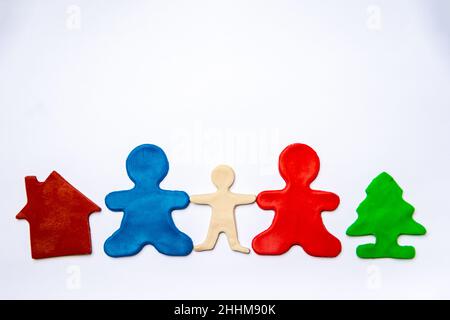 Due uomini di plastilina rossa e blu, come genitori, tengono la mano di un bambino di plastilina bianca, una casa di plastilina, albero di plastilina verde su un backgroun bianco Foto Stock