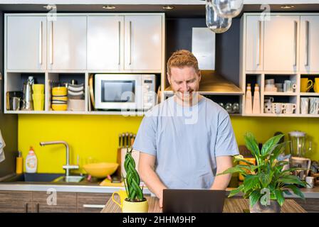 Ritratto di un giovane imprenditore di successo che lavora da casa a casa accogliente tavolo da cucina utilizzando computer portatile fare lavoro facendo chiamata online incontrare Foto Stock