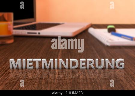 Mietminderung - parola tedesca per la riduzione di affitto - lettere su scrivania in legno con computer portatile e un notebook. 3d rappresentazione illustrazione. Foto Stock