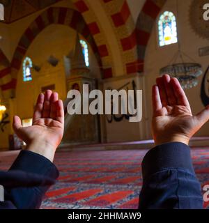 Sfondo islamico. L'uomo musulmano che prega alzando le mani nella moschea. Testo del nome di Allah sulle pareti. Foto di sfondo Ramadan o islamica. Ed Foto Stock