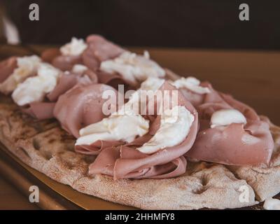 Primo piano tagliere in legno con tipica Pinsa Romana in cima ricoperta di mozzarella e mortadella Foto Stock