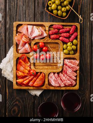 Spuntini per vino su un asse di legno. Menazhnitsa con salsiccia, olive e pomodori ciliegini. Foto Stock