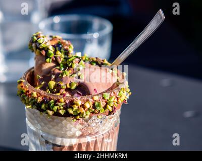 primo piano tazza di vetro con gelato al cioccolato e pezzi di pistacchio come decorazione Foto Stock