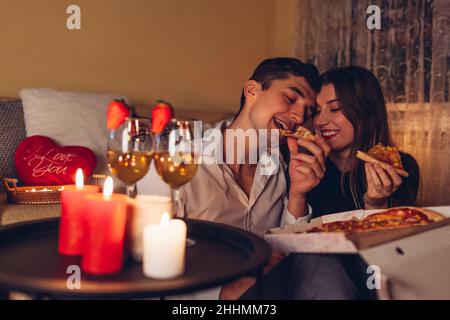 San Valentino coppia in amore mangiare pizza bere vino con fragole avere cena romantica celebrare a casa di notte Foto Stock