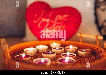 Decorazione d'interni del giorno di San Valentino a casa. Molte piccole candele che bruciano su vassoio da cuore rosso a forma di cuscino. Atmosfera romantica e accogliente. Primo piano Foto Stock