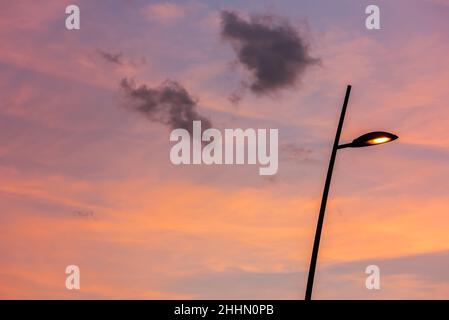 Lampada da strada con un cielo arancione al tramonto e nuvole di colore lilla su sfondo a cornice intera Foto Stock