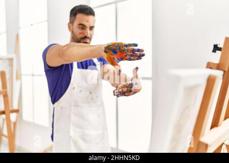 Giovane uomo ispanico che guarda tela disegnare facendo un gesto di foto con le mani in studio d'arte Foto Stock