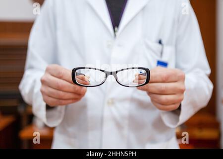 Un medico di occhio di sesso maschile in un cappotto bianco mostra un paio di occhiali correttivi per correggere miopia. Gli occhi hanno una cornice nera. Foto Stock