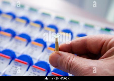 Un medico ottico mostra una nuova lente a contatto chiara e pulita appoggiata su un supporto bastone. Sullo sfondo ci sono molte confezioni di altre nuove lenti a contatto Foto Stock