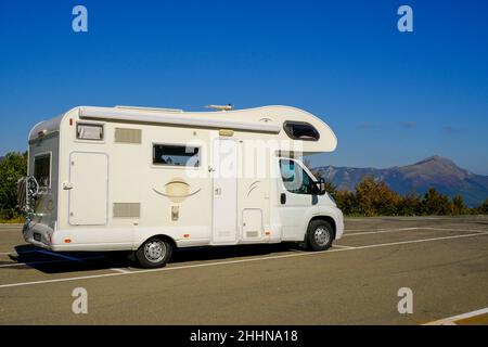 camper sulla strada attraverso il cielo blu e le vette delle montagne. Stile di vita avventuroso. Vita camper. Viaggi in montagna Foto Stock