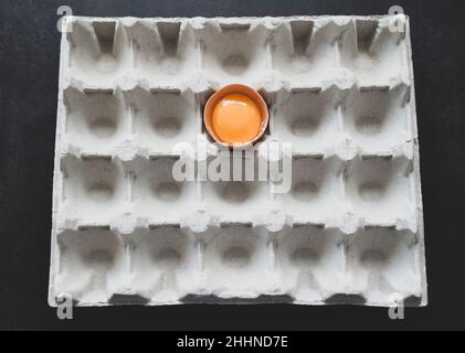 Metà dell'uovo fresco con tuorlo brillante in vassoio di carta per uova su sfondo nero. Vista dall'alto Foto Stock