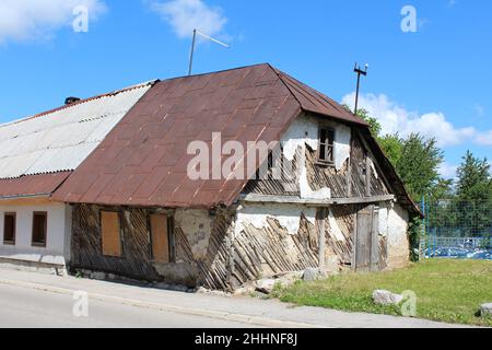 Piccola vecchia casa familiare suburbana abbandonata molto piccola fatta di legno e materiali naturali argillosi con facciata dilatata e incrinato Foto Stock