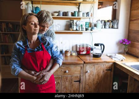 Romantica coppia caucasica matura abbracciando da cucina bancone in casa. Semplice vita, convivenza, stile di vita e amore. Foto Stock