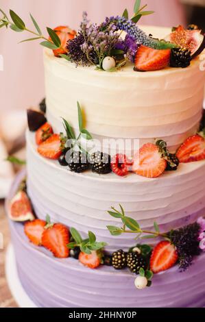 Torta nuziale a tre livelli luminosa. Torta bianca cremosa decorata con frutta di fesh, bacche e fiori. Foto Stock