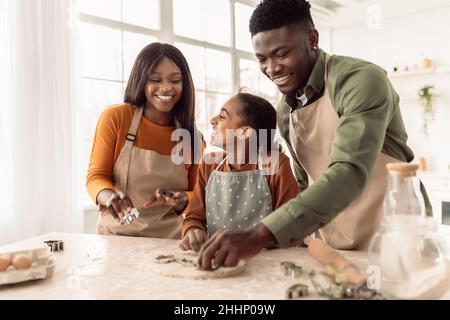 Famiglia nera che usa le forme di cottura che fanno i biscotti in cucina Foto Stock