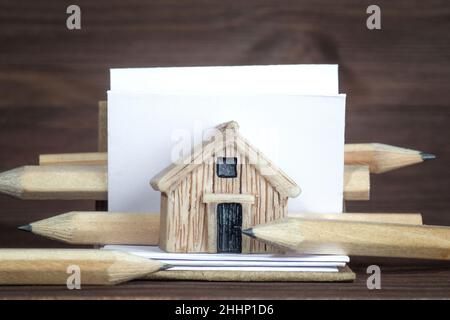 Casa in miniatura, libro di schizzo aperto e matite su sfondo di legno. Progetto di costruzione di alloggi. Foto Stock