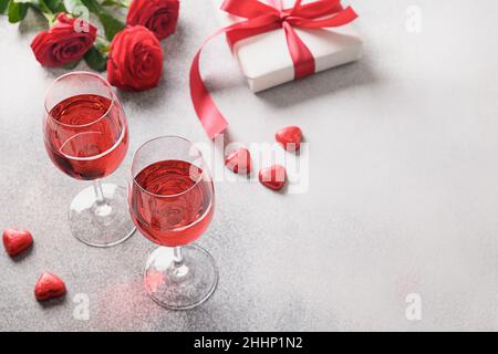 Due bicchieri di vino con vino rosso per incontri romantici o cena di San Valentino con fiori di rosa rossa su sfondo grigio. Spazio di copia. Primo piano. Foto Stock