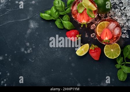 Cocktail punch. Due bicchieri di punch e ingredienti freschi per la produzione di limonata, acqua di disintossicazione infusa o cocktail. Fragole, lime, menta, basilico, ghiaccio Foto Stock