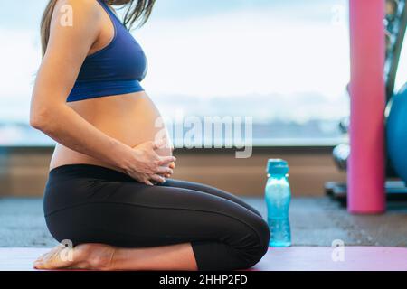 Donna incinta che tocca il ventre mentre si esercita in palestra. Sport durante la gravidanza Foto Stock