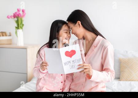 Sorridendo bella giapponese giovane femmina e ragazza teen in pigiama rosa tenere carta, godere del tempo insieme a letto Foto Stock